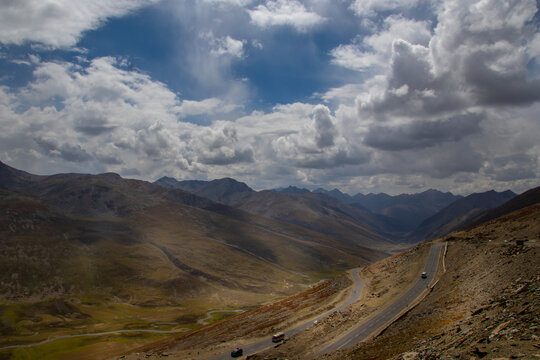 View of the winding road leading towards Nanga Parbat, surrounded by the rugged mountain landscape of the Gilgit region under a dramatic cloudy sky in Fairy Meadow, Gilgit, Pakistan.