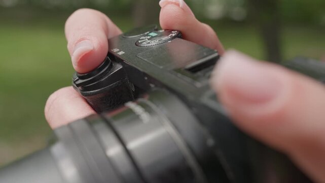Close up view shows hands adjusting settings for outdoor photography session with greenery in background. focus remains on digital SLR or mirrorless interchangeable lens camera highlighting
