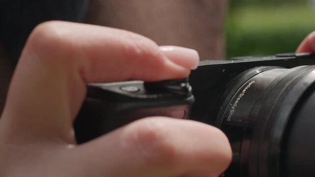 Close up view of hands adjusting settings on black digital SLR or mirrorless camera focusing lens and body details. Fingers press buttons near top left corner while another hand holds part