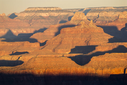 View of the Grand Canyon with rugged red rock formations and deep shadows cast by the golden hour light in Coconino County, Arizona, United States.