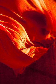 View of the smooth, flowing sandstone walls of Antelope Canyon with vibrant orange and red light patterns reflecting off the rock surfaces in Coconino County, Arizona, United States.