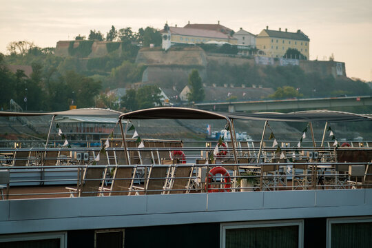View of the deck of a river cruise ship with lounge chairs and flags, with the historic Petrovaradin Fortress visible in the background in Novi Sad, Vojvodina, Serbia.