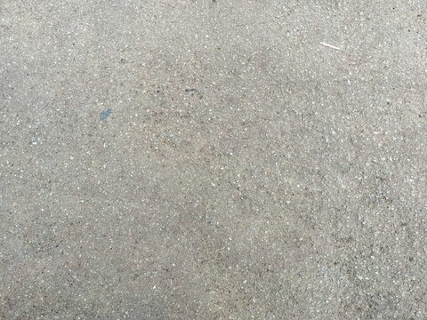 Close-up of rough gray asphalt surface with fine gravel grains and subtle speckles, creating a coarse, weathered texture suitable for urban backgrounds and construction themes.