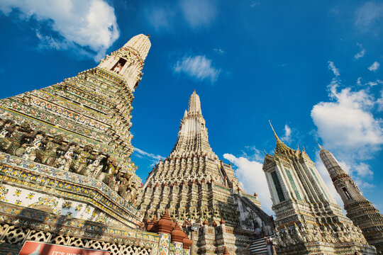 View of the ornate spires of Wat Arun temple decorated with colorful porcelain mosaics under a bright blue sky in Wat Arun, Bangkok, Thailand.