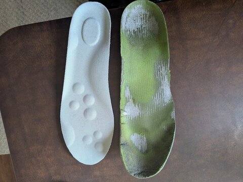 Comparison of a new white foam orthotic shoe insert next to a heavily worn, green-patterned arch support insole, highlighting long-term foot care and equipment replacement.