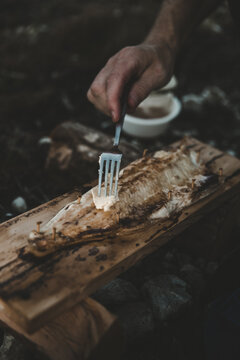 View of a person placing butter on a piece of plank-grilled fish on a wooden board in Laane County, Estonia.