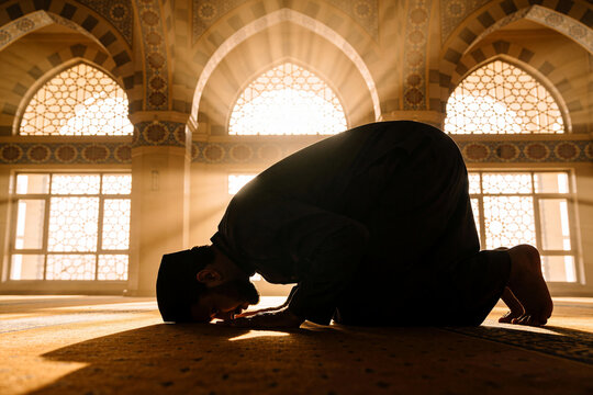 Muslim man in sujud prostration praying inside mosque with golden sunbeams background