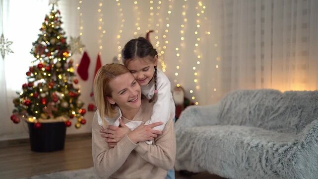 Happy young daughter affectionately hugging her mother from behind in a cozy Christmas-decorated room