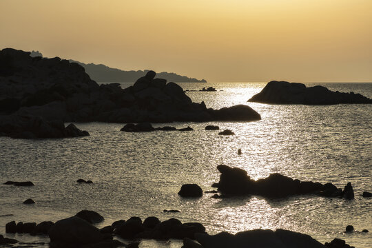 View of Bassa Trinita Beach with rocky coastline and calm sea at sunset in La Maddalena, Sardinia, Italy.