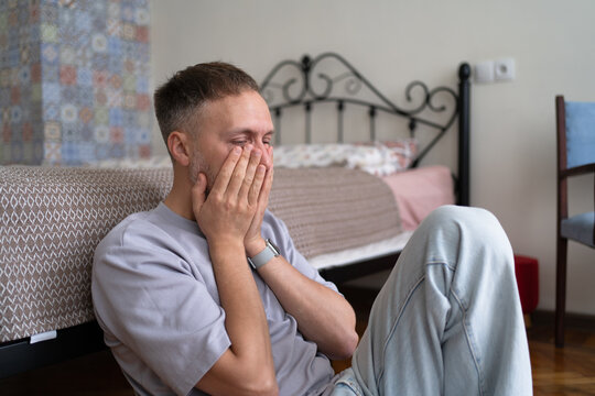 Stressed man on floor rethinks life crisis with emotional exhaustion and anxiety at home, overwhelmed by uncertainty, difficult choices and midlife transition.