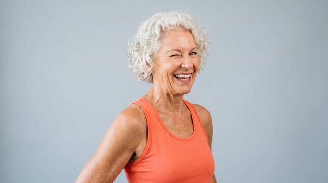 Senior content creators share their lifestyle online. A playful older woman winks and points towards the camera in orange activewear.