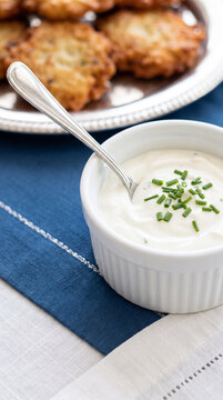 Sour cream dip with chives for latkes served in white bowl on blue napkin