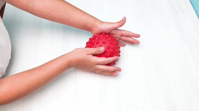 Child hands rolling red textured ball with massage spikes Concept of sensory integration pediatric physical therapy motor skills development tactile stimulation rehabilitation Acupuncture treatment