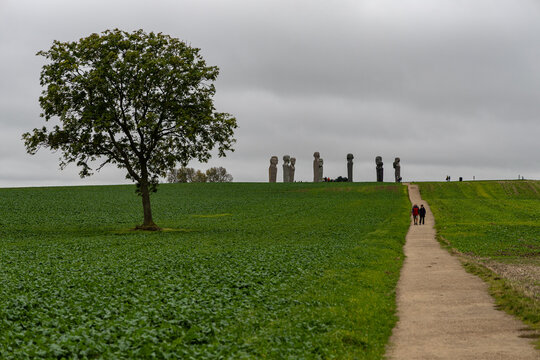 View of the Dodekalitten stone sculptures standing on a hill with a large tree in the foreground and a path leading towards them in Kragenaes, Lolland, Denmark.