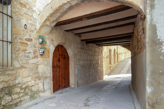 Pasadizo de piedra con puerta de madera y techo de vigas en Puertomingalvo, Teruel, reflejo del encanto medieval y la arquitectura tradicional de los pueblos hist&oacute;ricos de Espa&ntilde;a