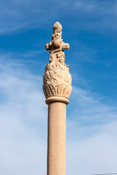 Columna de piedra tallada con cruz y motivos naturales bajo cielo azul, s&iacute;mbolo de arte, historia y espiritualidad en la arquitectura tradicional espa&ntilde;ola