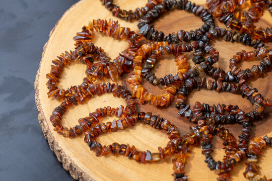 Multiple strands of polished amber chip bead necklaces in honey cognac and dark brown colors arranged in loops on a round wooden slice with bark edge, top view, warm natural jewelry still life