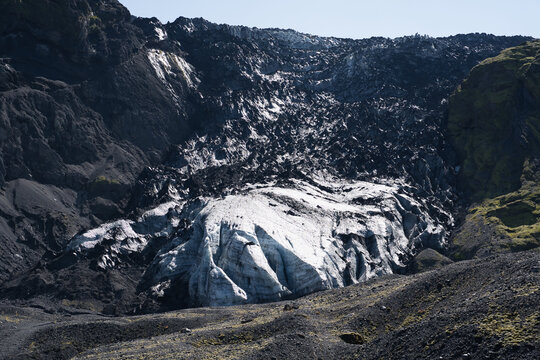 View of the Eyjafjallajokull glacier surrounded by rugged black volcanic rock and mossy slopes in Hvolsvollur, Rangarthing eystra, Iceland.