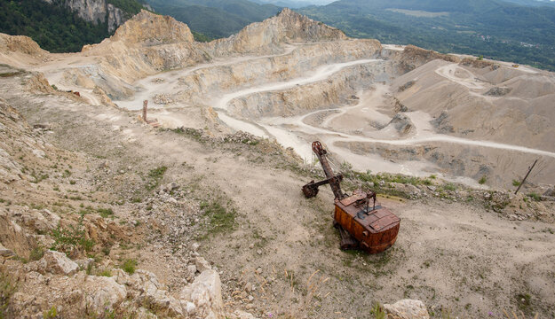 View of a rusty vintage excavator abandoned in a large open-pit limestone quarry surrounded by the rugged landscape of the Apuseni Mountains in Horea, Alba County, Romania.