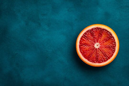A sliced blood orange rests on a dark teal textured background.