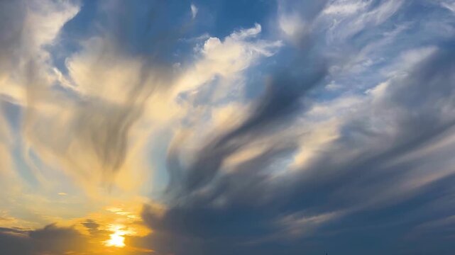 Setting sun disappearing behind the horizon with wispy cirrus clouds moving across a dramatic sky
