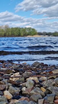 Rocky riverbank under cloudy sky. Scenic landscape, close-up of pebbles on the shore of a reservoir. Ecology, outdoor recreation and travel. Early autumn. View from ground level to the riverbank