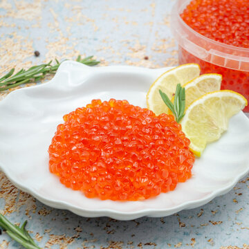 Fresh red salmon caviar served on white shell shaped plate with lemon slices and rosemary sprig