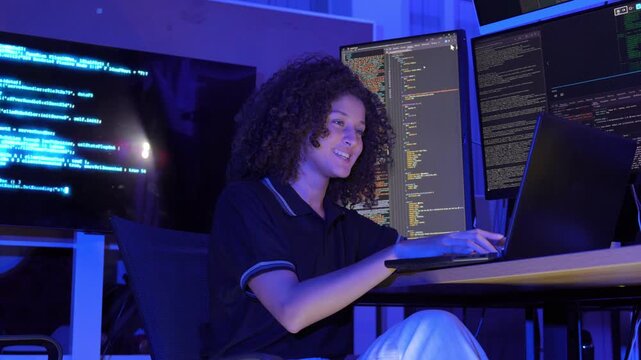 Female software developer working with multiple monitors display programming code in a modern technology workspace. coding, cybersecurity, digital technology, data processing, programming, innovation.