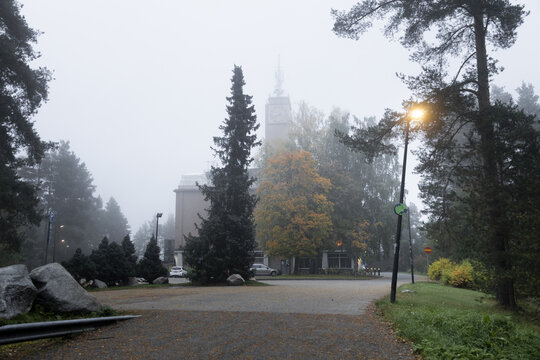 View of a building with a clock tower surrounded by pine trees and autumn foliage in a foggy park setting in Jyvaskyla, Central Finland, Finland.