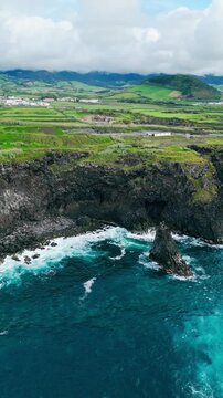 Aerial view of rocky volcanic coastline on Sao Miguel Island, Azores, Portugal, with Atlantic Ocean waves, steep cliffs, eroded headlands and green coastal fields near shore