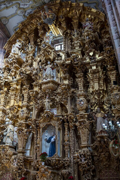 View of the ornate golden baroque altarpiece with intricate wood carvings and religious statues inside a historic church in Guanajuato, Guanajuato, Mexico.
