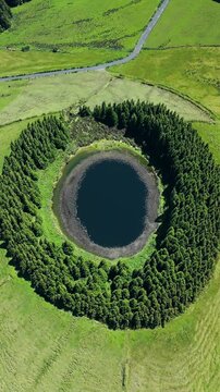 Circular crater lake on Sao Miguel Island, Azores, Portugal. Vertical aerial footage of Lagoa do Pau Pique surrounded by forest and green pastures