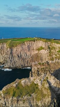 Rocky cliffs drop steeply toward Atlantic Ocean on Sao Miguel, Azores, Portugal. Close aerial footage along towering coastal rock