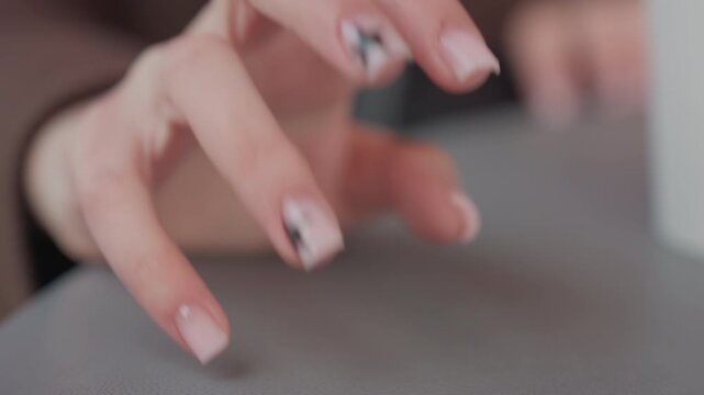 Woman hands rest on smooth surface. Her fingernails are painted light pink and feature black star designs. scene is softly lit emphasizing nail art details