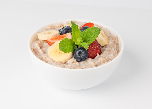 Cooked spelt in bowl isolated. Oatmeal milk porridge with fruits and berries