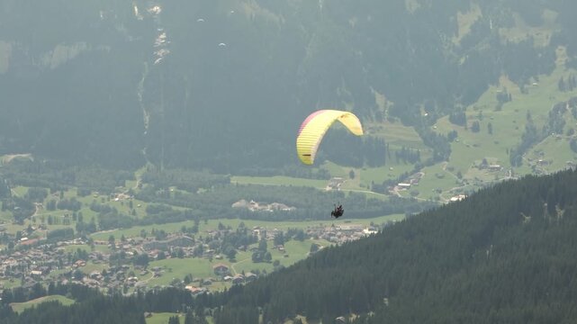 Tandem paragliding flight over a Swiss mountain village, Alps, Switzerland. Professional pilot and passenger flying above scenic alpine landscape. Adventure tourism, outdoor recreation and freedom.