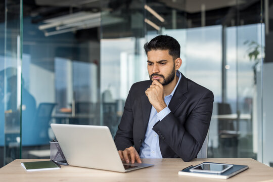 Young businessman thinking and working on laptop in modern office