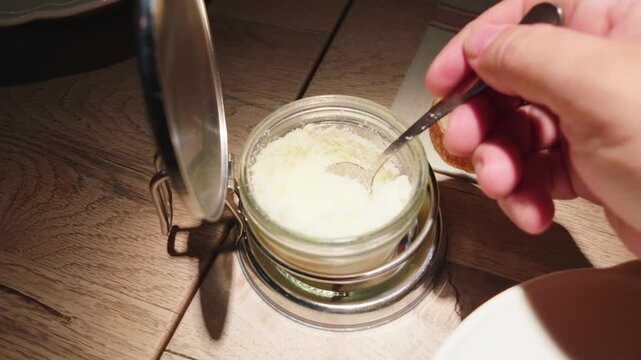 Person sprinkling grated parmesan cheese on spaghetti carbonara