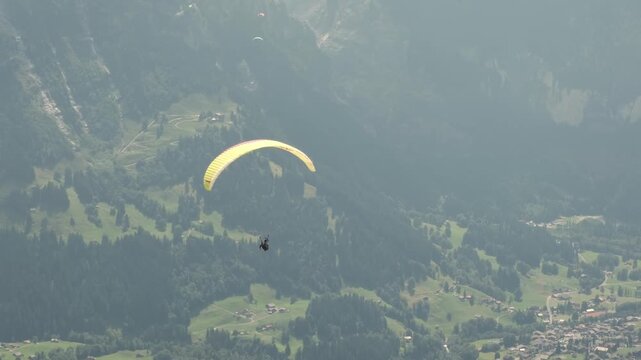 Tandem paragliding flight over Grindelwald near First mountain, Switzerland. Professional pilot and passenger flying above scenic alpine landscape. Concept of adventure tourism, outdoor recreation.