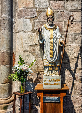 Dol de Bretagne, France, Europe - August 6, 2026: The Saint Samson Cathedral. Wooden sculpture of Saint Samson against the old wall. Bouquet of flowers