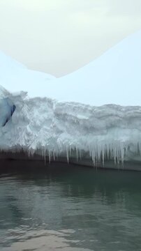 Vertical Video of Snowy Mountain Ridge Beyond Floating Ice. White ice, rippling water and snow-covered ridges create a layered cold seascape beneath soft diffuse light.