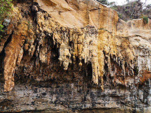 Close-up of yellow and orange limestone cliff with dripping stalactite-like flowstone formations