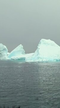 Vertical Video of Jagged Distant Icebergs Along the Horizon. White and blue ice, rippling water and soft diffuse light reveal natural frozen texture and sculpted contours across the marine scene.