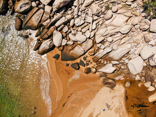Aerial view of smooth granite boulders, golden sand and clear shallow water on a small beach with tiny people, Magnetic Island, Australia © Florian
