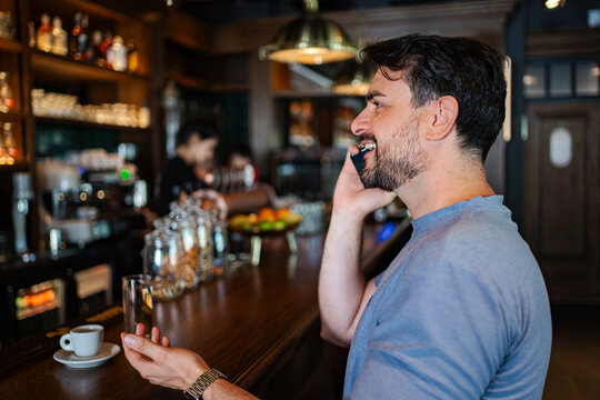 Man talking on mobile phone while sitting at a bar drinking espresso