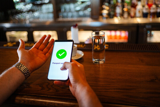 Person's hand holding smartphone displaying vaccine verification in a bar
