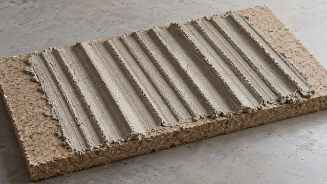 Applied tile adhesive mortar with notched trowel ridges on insulation board. Concept of mineral paste, construction, cement, plaster, tile glue, thinset, building material. Copy space.