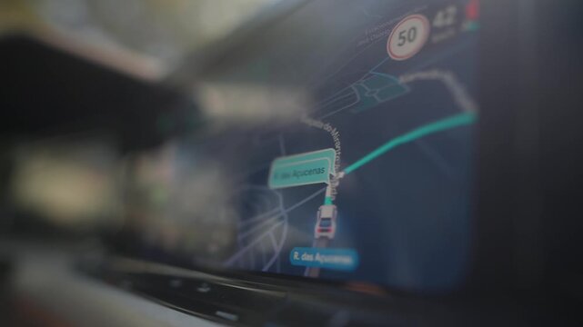 In-car oblique close view of touchscreen navigation display refocusing on route, with vehicle position marker and speed limit 50 visible on screen during driving