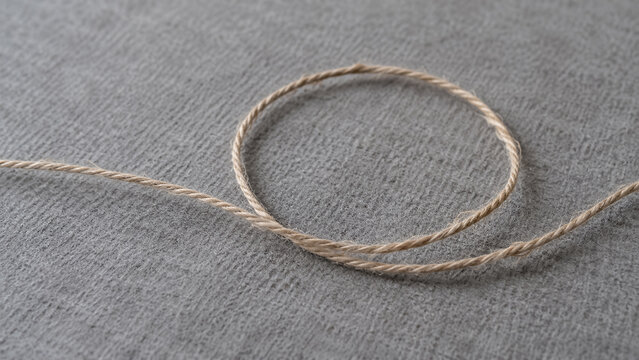 Thin natural linen twine cord forming a round loop on gray textured fabric background. Concept of string, rope, jute, craft. Copy space.