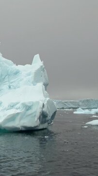 Vertical Video of Clustered Blue Icebergs Across Dark Water. White and blue ice, rippling water and soft diffuse light reveal natural frozen texture and sculpted contours across the marine scene.